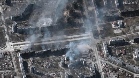 satellite photo of smoke rising from buildings in a neighborhood that has been destroyed by bombing