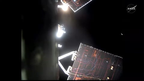 The Artemis II Orion spacecraft and its solar arrays appear in the foreground, with a sliver of Moon showing in the black background of space.