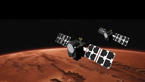 An illustration showing two large satellites with solar arrays on either side floating above the reddish-brownish surface of Mars.