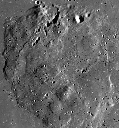 Overhead satellite mosaic showing Mons Rümker, a large, rounded volcanic mound on the Moon's surface surrounded by flat, dark lunar plains. The terrain is marked with impact craters of various sizes, with sharp sunlight casting deep, dark shadows along crater rims and the bumpy, elevated boundaries of the volcanic feature.