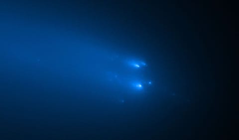 The comet breaks apart into several bright, fuzzy, blue, streaking lights in a line from left to right on a black background.