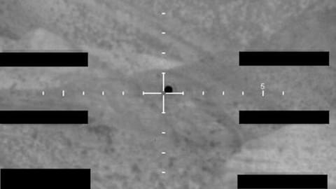 a dark blob seen against a mountainous desert landscape in a monochromatic, grainy photograph