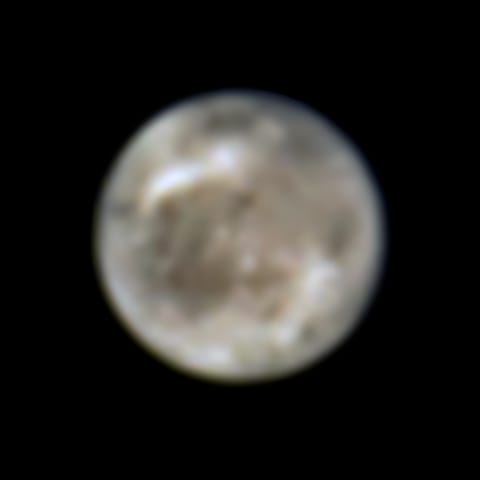 A hazy, out-of-focus sphere of a moon, gray-brown with large white streaks and smaller off-white patches.