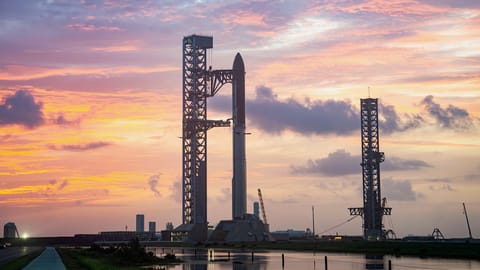 a giant rocket stands on a launch pad against a sunset sky