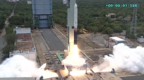 a blue and white rocket launches against a backdrop of trees