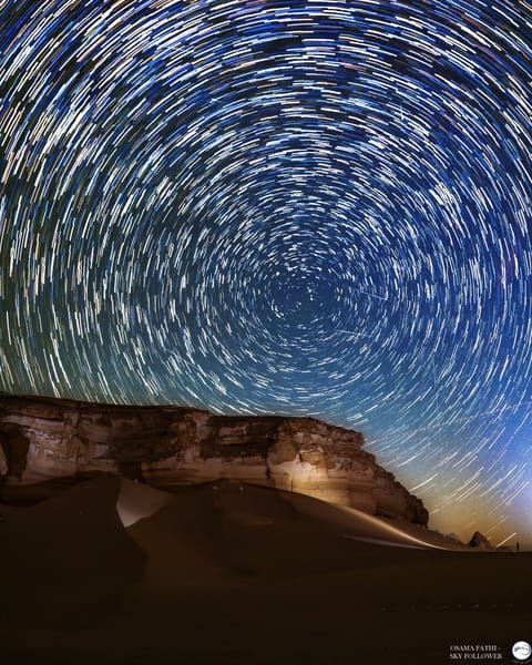 Star trails circle above a desert at night as meteors streak through the sky.