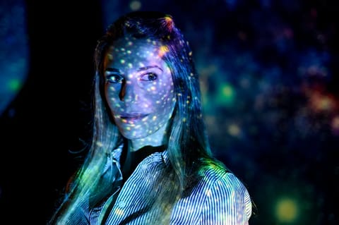Jacqueline McCleary, associate professor in the College of Science, facing forward with patterns of light resembling stars and galaxies projected across her face and hair.
