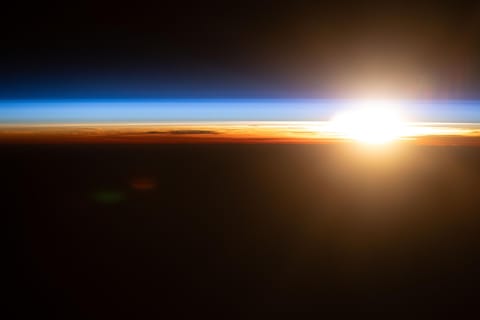 An orbital sunrise above the Pacific Ocean illuminates Earth's atmosphere, revealing cloud tops and orange and blue hues outlining the planet's horizon. The International Space Station was orbiting 263 miles above the Hawaiian island chain at approximately 4:09 a.m. local time when this photograph was taken.