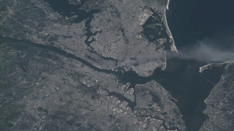 satellite photo of a large city on a bay, with a river running through it and smoke rising from the center of the city